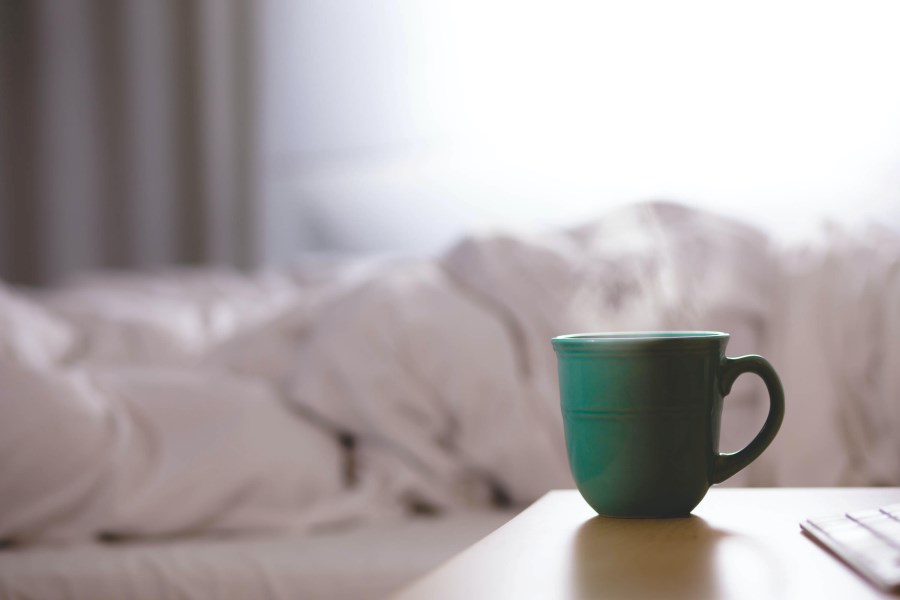 Tasse Tee auf Nachttisch neben Bett