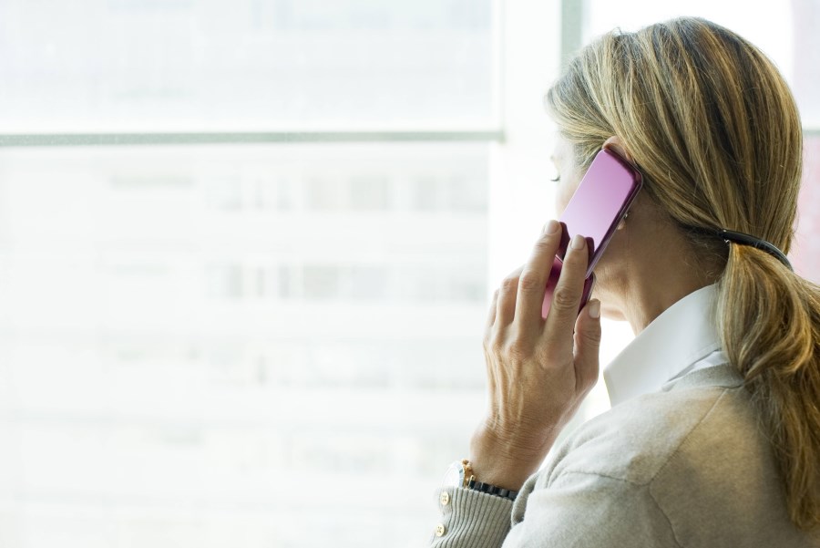 Frau telefoniert mit Handy und blickt aus Fenster