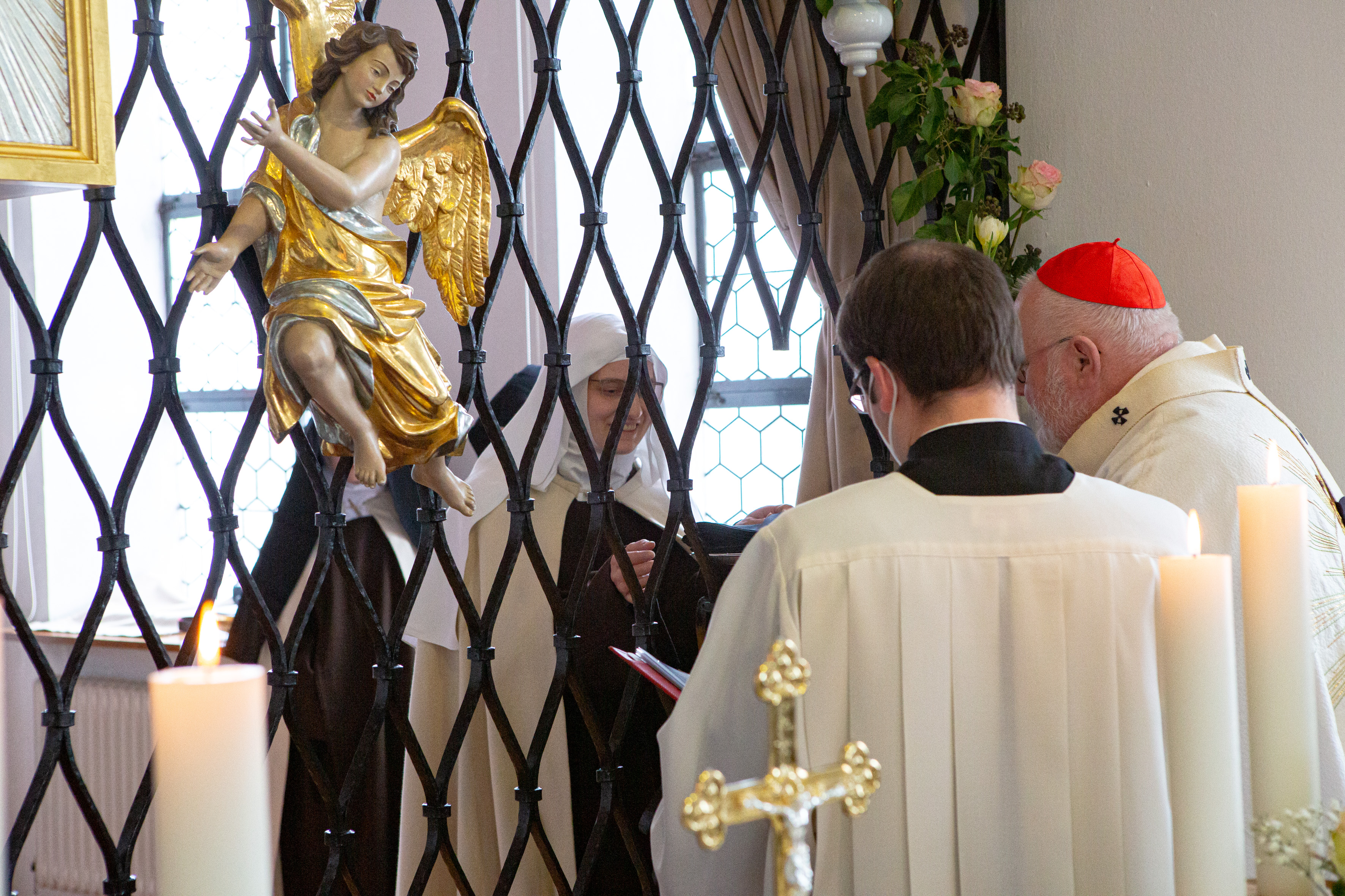 Kardinal Reinhard Marx reicht Sr. Margareta den geweihten Schleier durch das Kommuniongitter