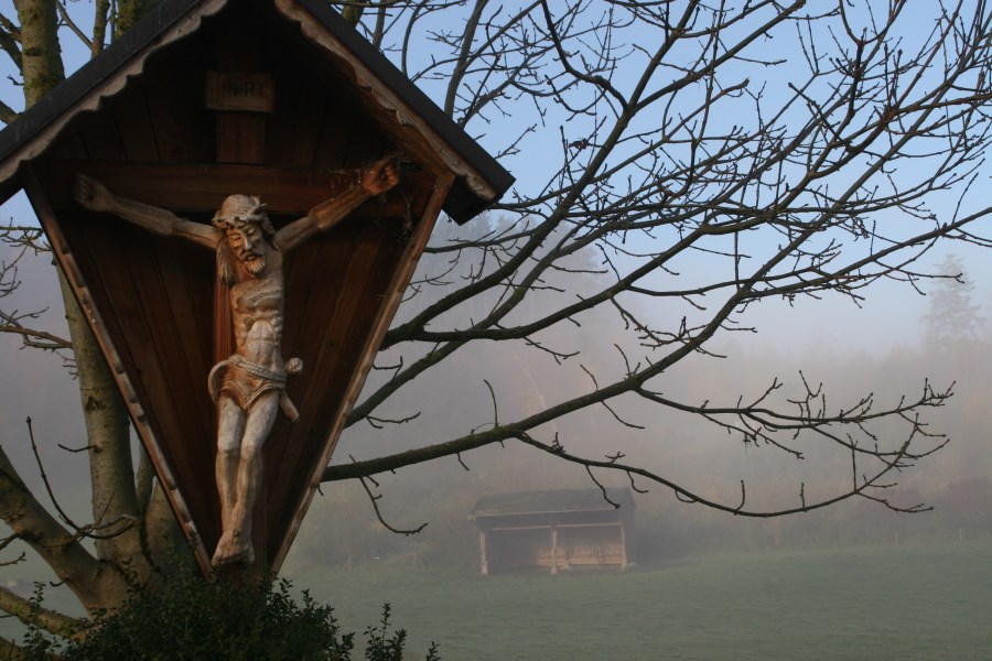 geschnitzes Holzkruzifix in einer nebeligen Herbstlandschaft