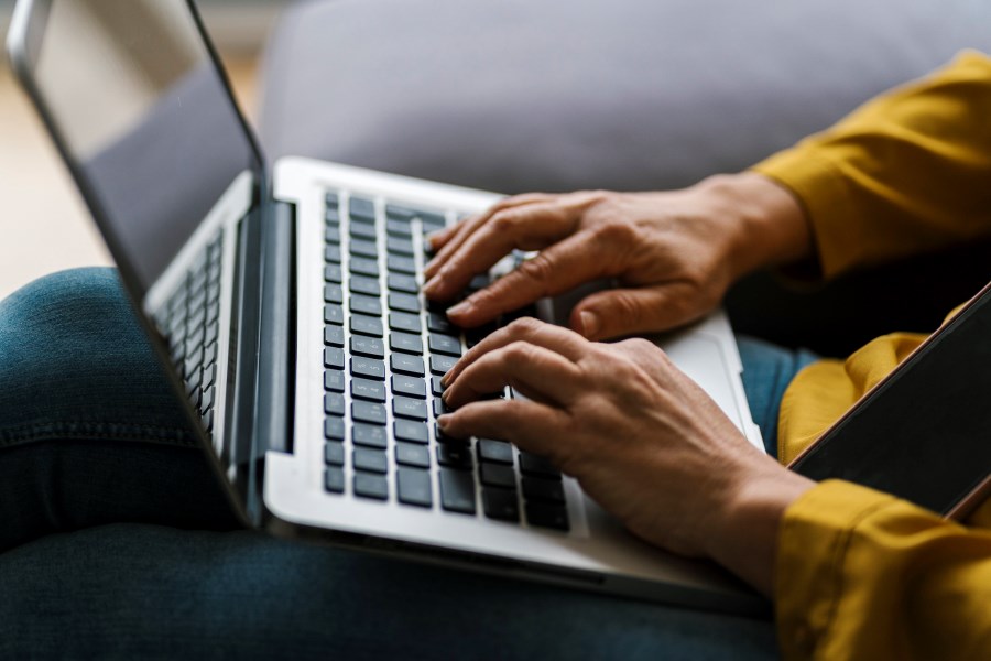 Hände tippen in Laptop auf dem Schoß