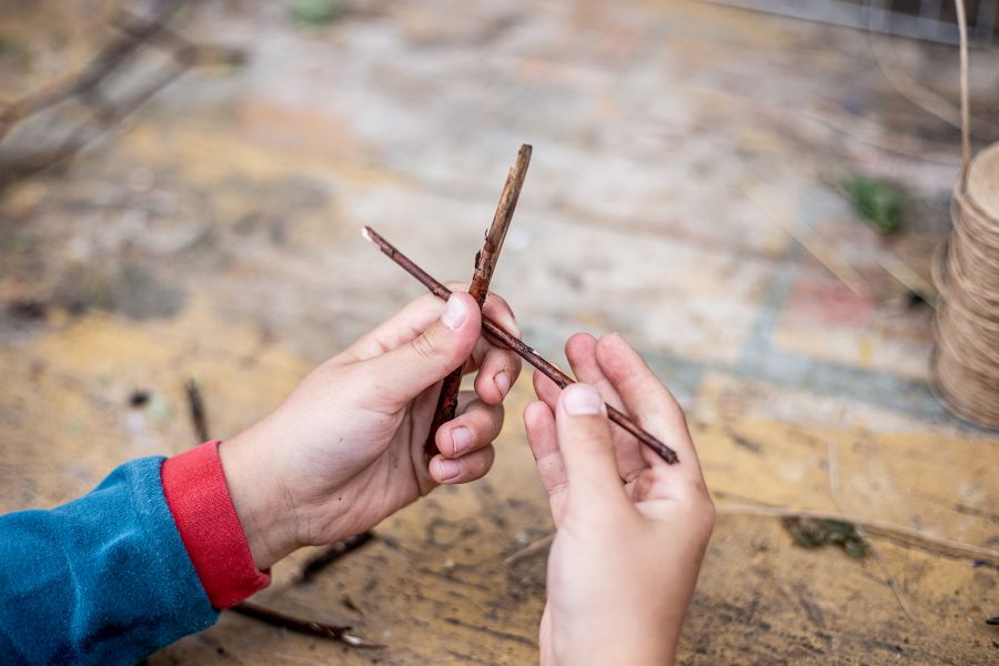 Kind legt zwei kleine Holzäste zu einem Kreuz übereinander