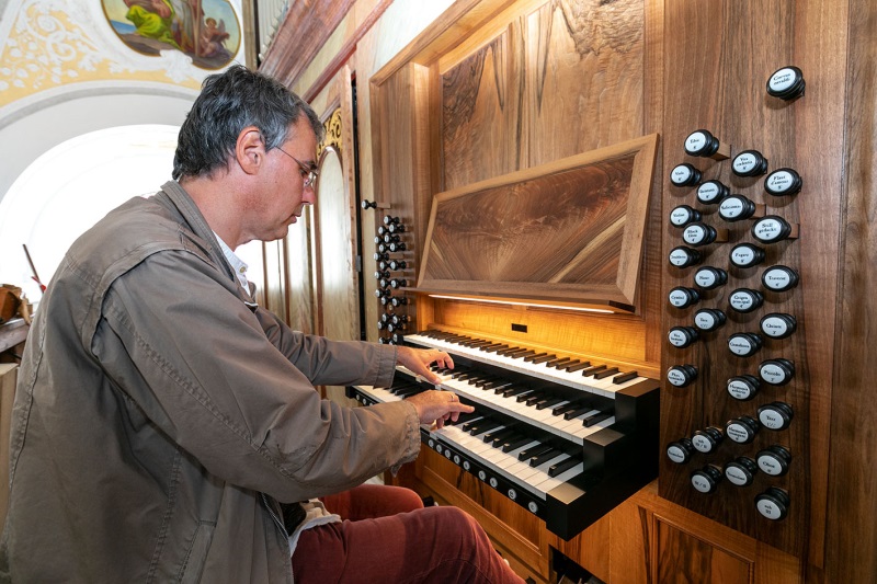 Kirchenmusiker Manfred Müller am Spieltisch der neugebauten Hauptorgel des Papst-Benedikt-Orgelwerks in der Stadtpfarrkirche St. Oswald mit Klaviaturen und Registerzügen.