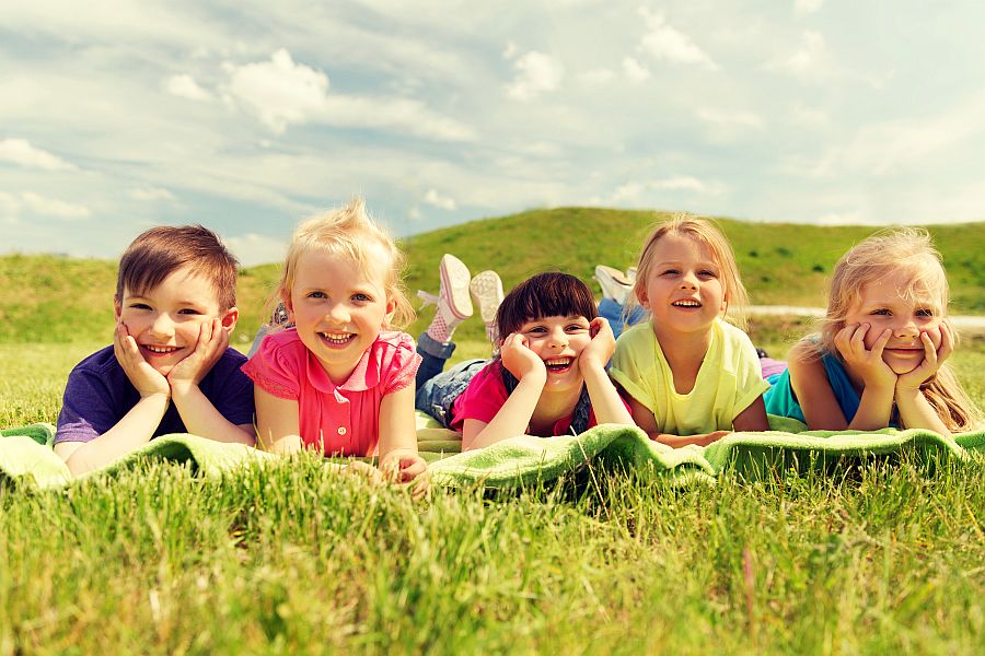 Kinder liegen nebeneinander auf Wiese und lachen