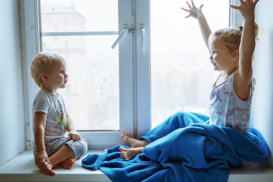Auf dem Foto sind zwei Kinder auf einer Fensterbank zu sehen.