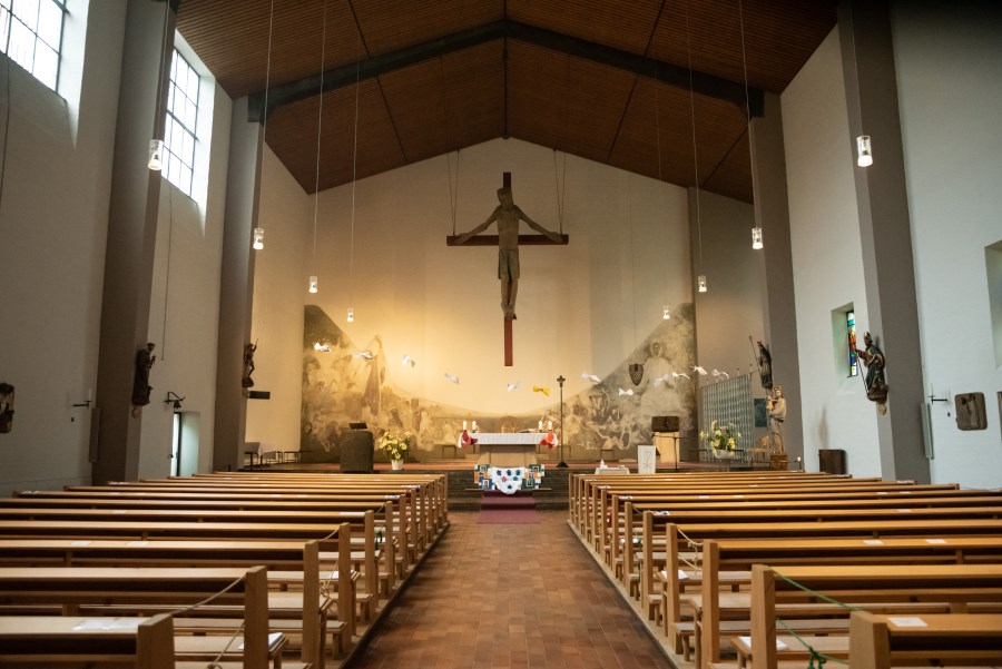 Blick durch Kirchenschiff zum Altar, darüber hängendes Kreuz