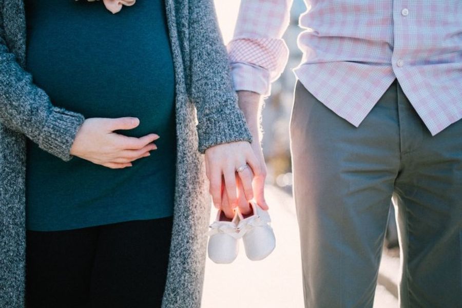 schwangere Frau und Partner halten gemeinsam Babyschuhe in den Händen