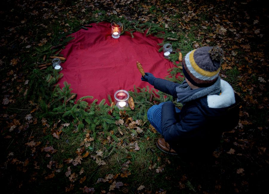 Kind an der Andachtstelle mit Kerze auf rotem Tuch im Wald
