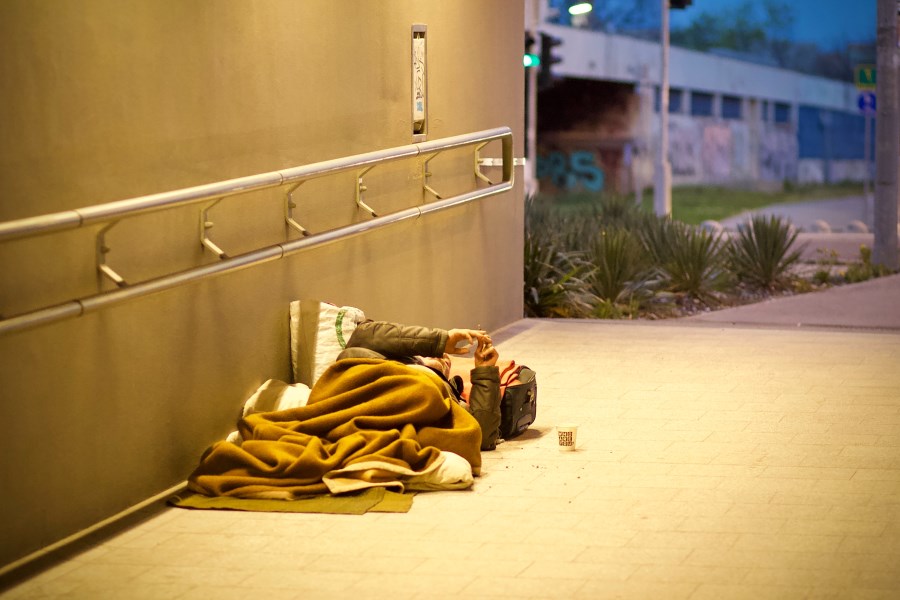 Auf dem Foto ist ein obdachloser Mann zu sehen, der in einer Unterführung auf einer Decke liegt.