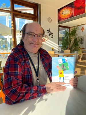Auf dem Foto ist ein ehemaliger wohnungsloser Mann zu sehen. In der Hand hält er das Kinderbuch "Über das Wünschen".