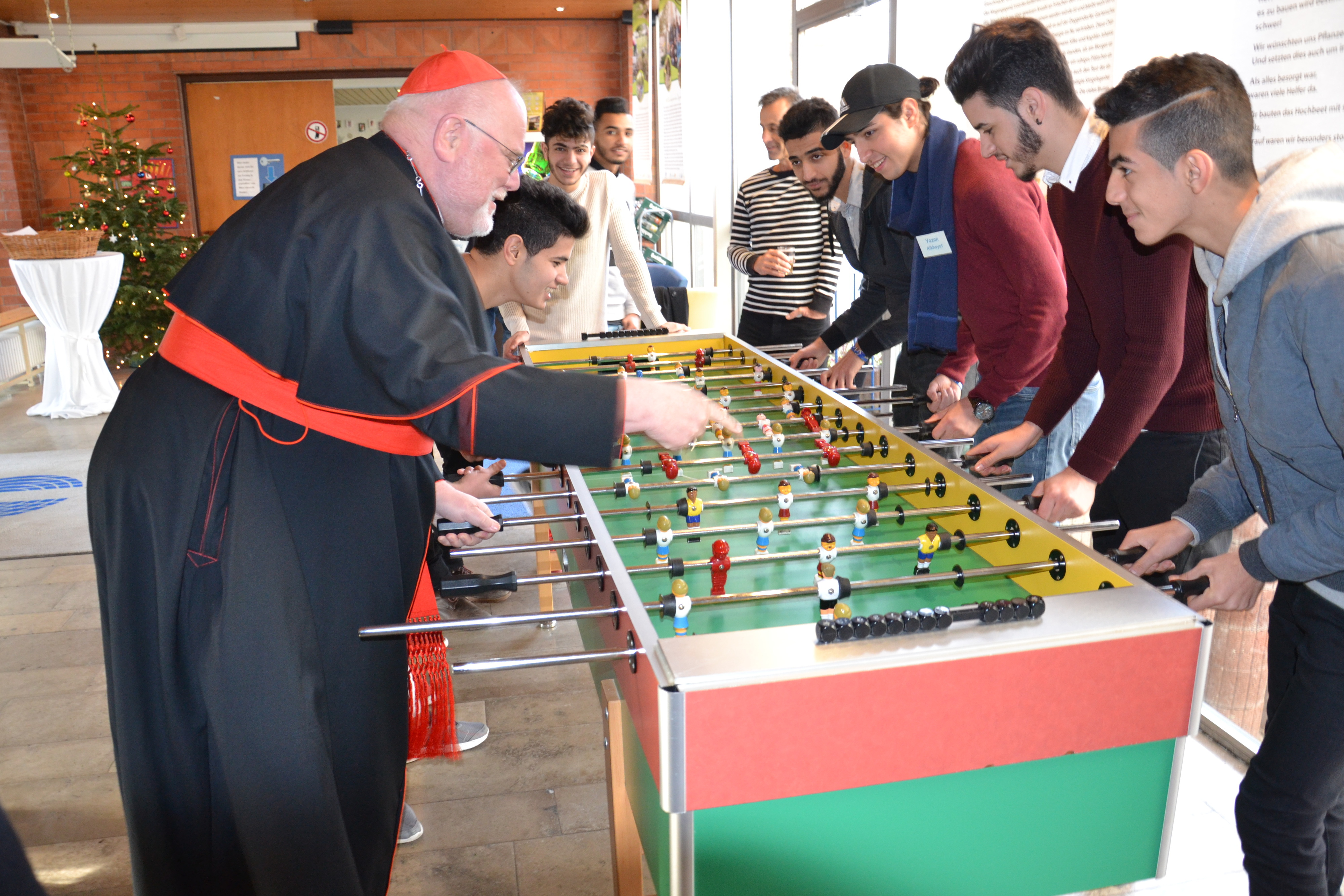 Auf dem Foto ist Kardinal Marx zu sehen, der im Jugendwohnheim Landshut des Katholischen Jugendsozialwerks mit jungen Geflüchteten Kicker spielt.