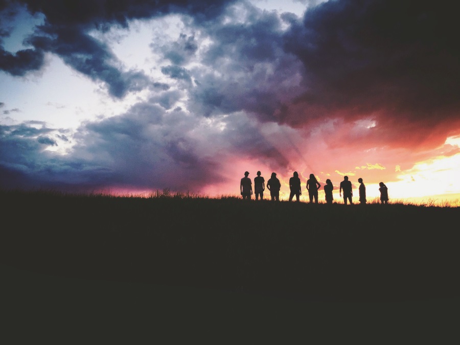 Auf dem Foto ist eine Gruppe Jugendlicher auf einem Berg zu sehen. Die Sonne geht gerade unter.