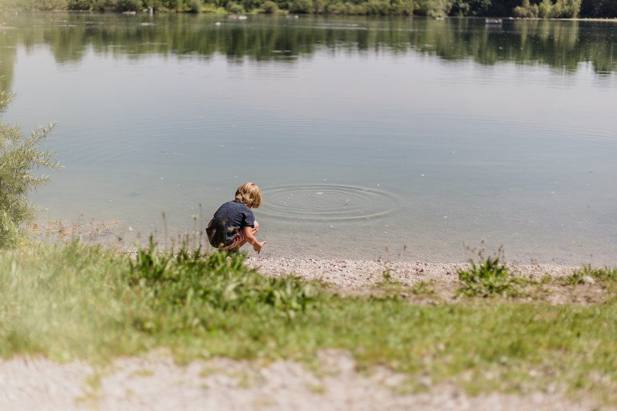 Kind wirft Stein ins Wasser
