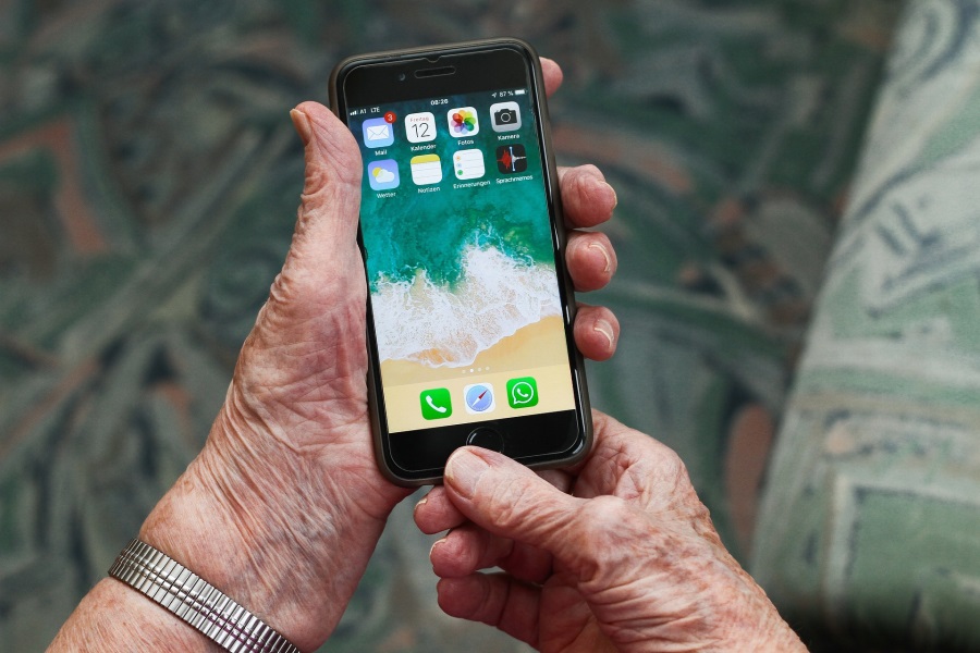 Auf dem Foto ist eine Hand einer älteren Person mit einem Smartphone zu sehen. Digitalbegleiter