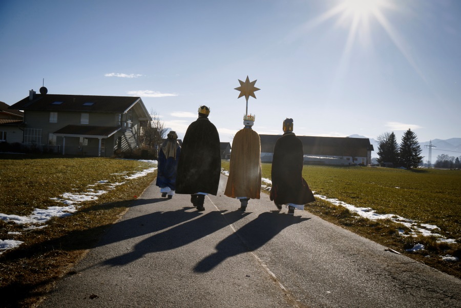 Kinder als Sternsinger verkleidet laufen über Feldweg bei Sonnenscheint in einen Ort