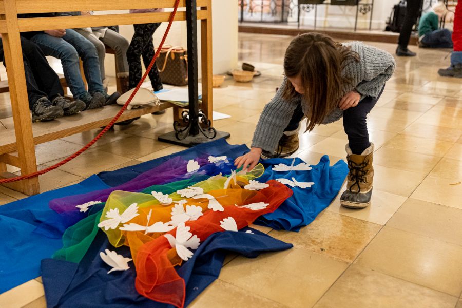Eine Schülerin der Klasse 1b der Franziskus-Grundschule legt eine Papier-Taube auf die Friedensfahne im Bürgersaal der Unterkirche