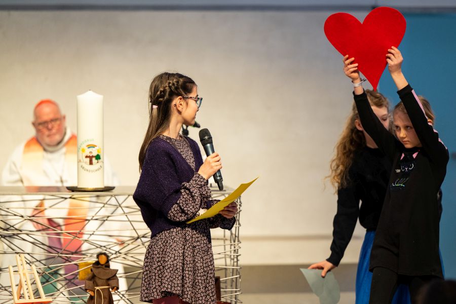 Eine Schülerin der Franziskus-Grundschule hält ein Herz hoch im Wortgottesdienst in der Campuskirche