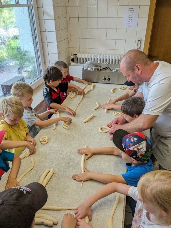 KiGa Besuch in der Bäckerei Fechner in Münchsdorf - Kinder am Tisch mit Teig beim ausrollen und formen