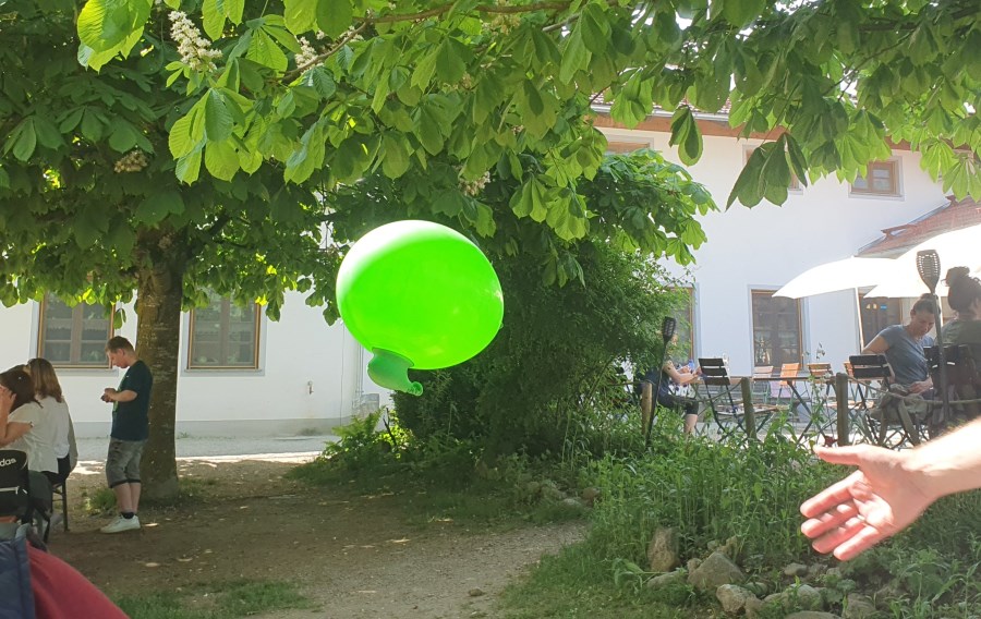 Ein fliegender grüner Luftballon, der nach unten eine Ausbuchtung hat und dadurch aussieht wie ein Zeppelin