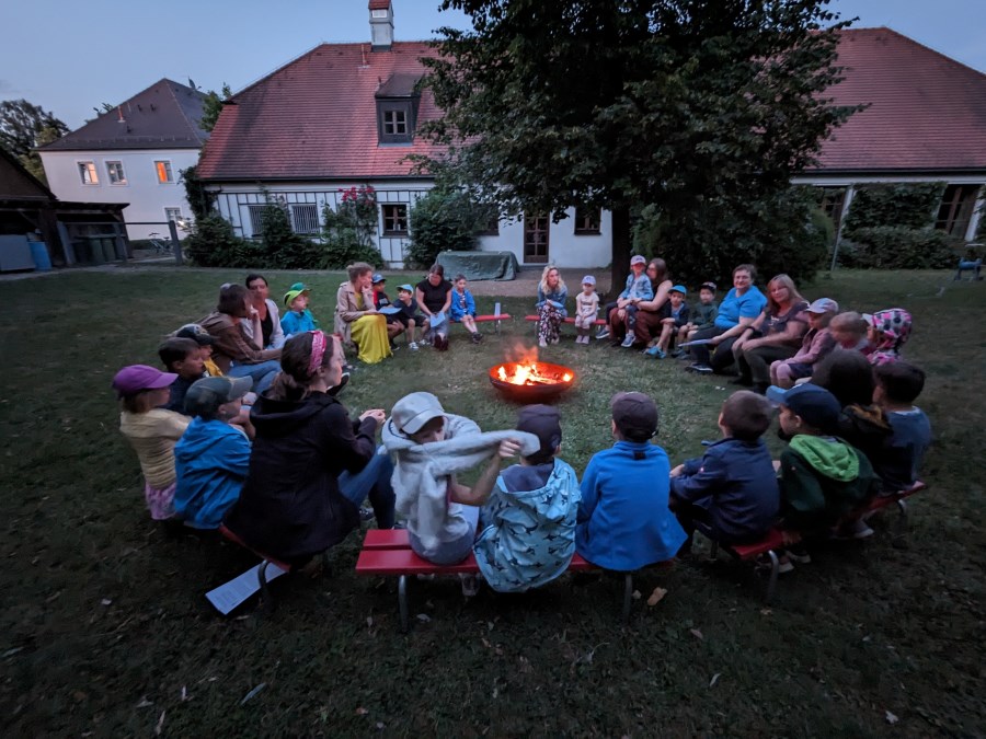 Im Kreis um eine Feuerschale sitzen die Vorschulkinder in der Dämmerung