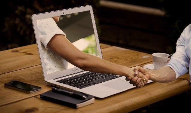 Digitales Pfarrbüro: Eine Hand streckt sich aus einem Laptop und schüttelte die Hand der Person vor dem Laptop