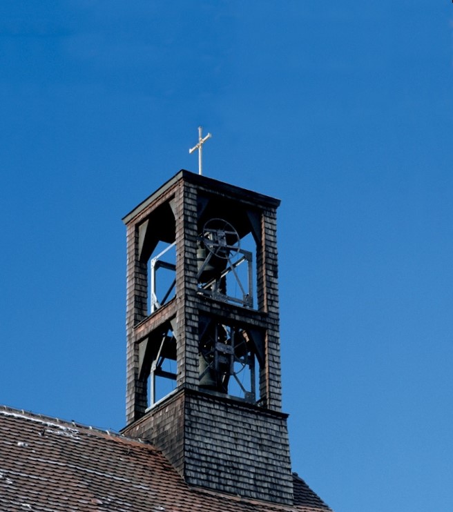 Kirchturmspitze mit Kreuz und Glocken vor blauem Himmel