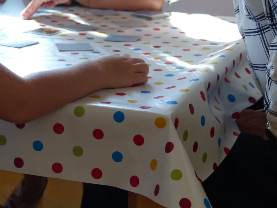 Memorykarten auf einem Tisch mit bunt betupfter Tischdecke, ein Kinderarm