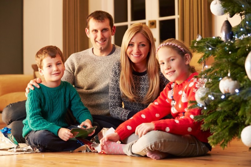 Auf dem Foto ist eine Familie mit zwei Kindern zu sehen, die vor einem Weihnachtsbaum sitzt.