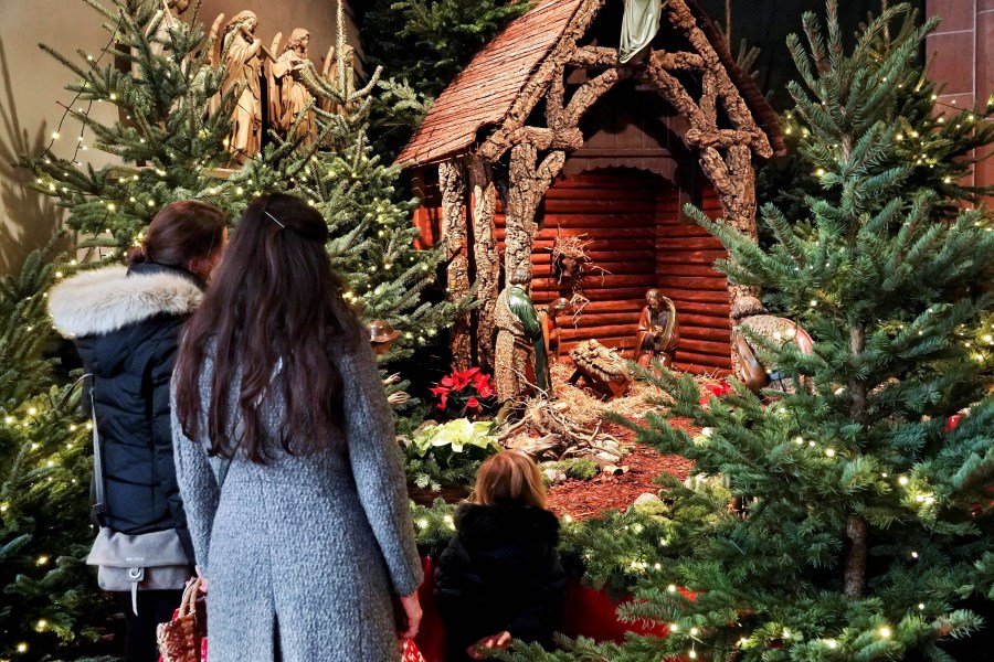 Auf dem Foto ist eine Familie zu sehen, die vor einer Weihnachtskrippe in einer Kirche steht.