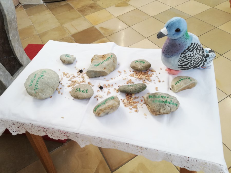 Taube aus Plüsch mit Körnern und Steinen auf einem Tischchen