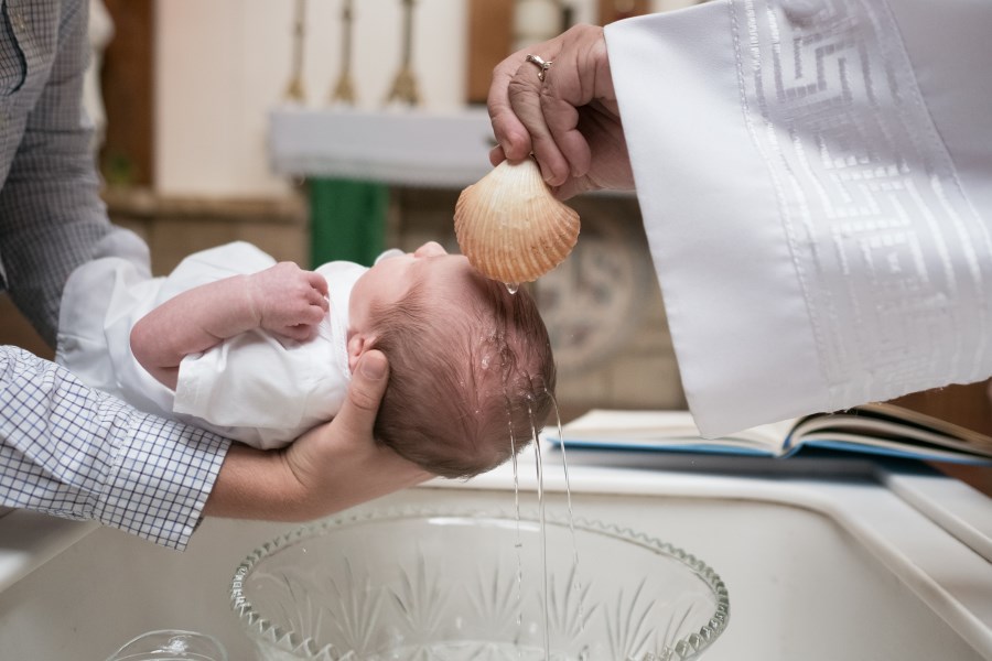Auf dem Foto ist an Baby zu sehen, das getauft wird.