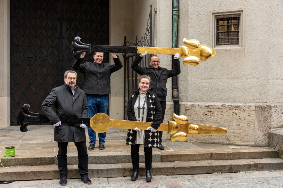 Mitarbeiter des Baureferats und der Kirche halten Zeiger vom Alten Peter hoch