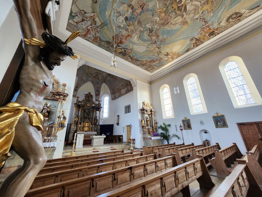 Blick in Kirchenraum mit Altären, Bänken, Fresko, links im Anschnitt Kruzifix