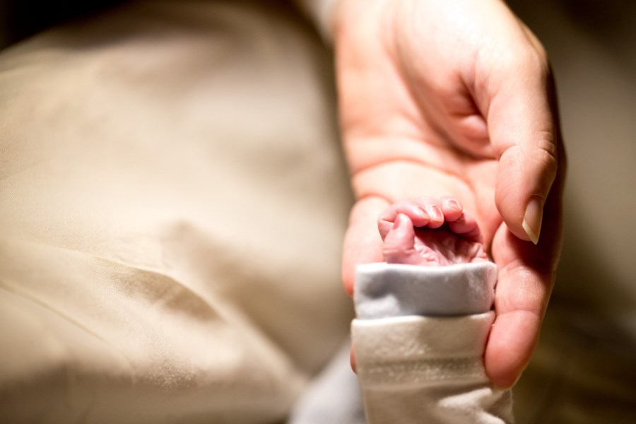 Auf dem Foto ist die Hand einer Mutter zu sehen, die die Hand ihres verstorbenen neugeborenen Kindes hält.
