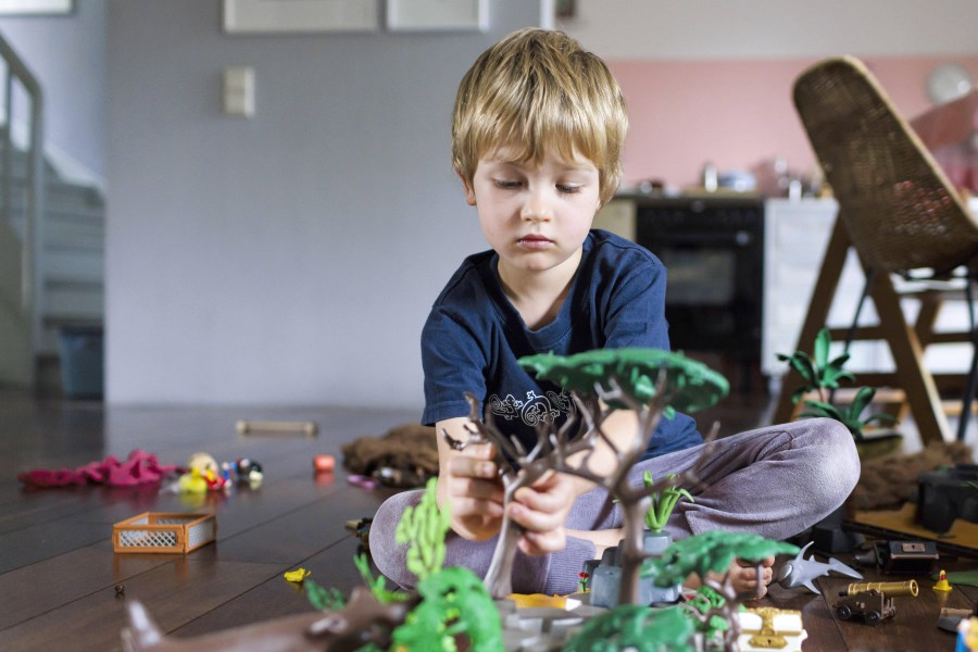 Auf dem Foto ist ein Junge zu sehen. Er spielt alleine Playmobil auf dem Boden.