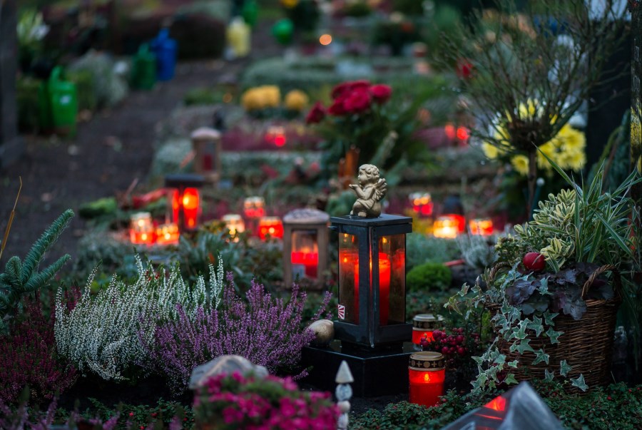 Auf dem Foto sind Gräber auf einem Friedhof zu sehen. Auf den Gräbern brennen Kerzen. Allerheiligen