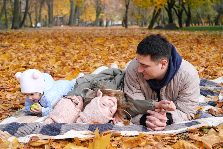 Auf dem Foto ist ein Familienvater zu sehen. Er liegt auf einer Decke mit seinen drei Kindern im Laubwald. Es ist Herbst. <br/>Alleinerziehend, verwitwet
