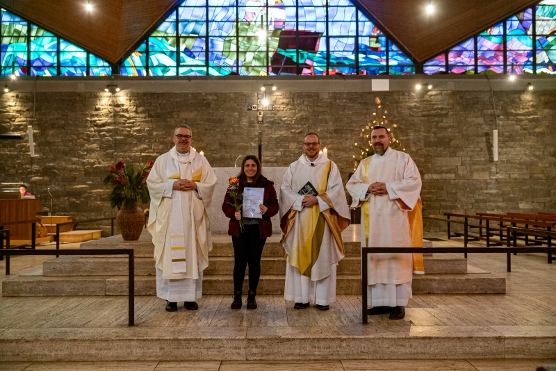 Marina Yusuf als neue Kommunionhelferin mit Urkunde und Blume vor dem Altar in St. Hildegard