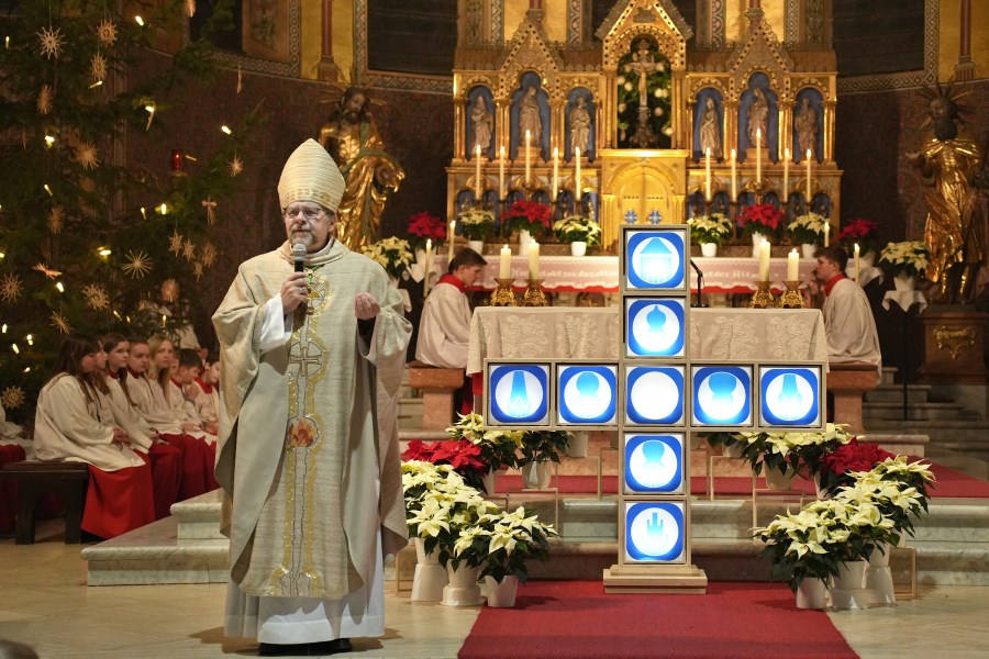Weibischof Wolfgang Bischof vor dem Symbol und Logo des neu gegründeten Pfarrverbandes Kraiburg-Flossing sieht den Zusammenschluss als ein Plus (+) für die Pfarreien und den Glauben.