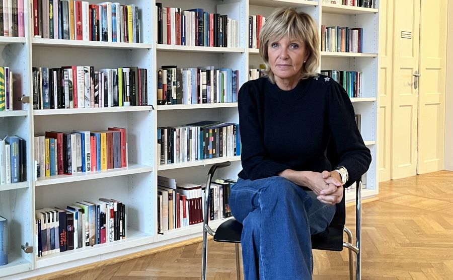 Ulrike Kriener sitzt auf einem Stuhl vor einem Bücherregal