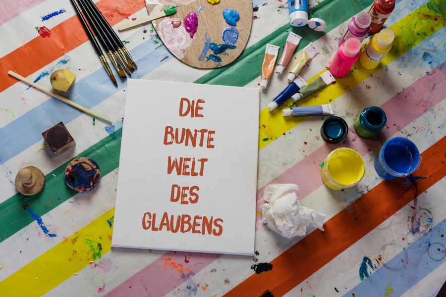 Tisch mit Malutensilien und einem Schild "Die bunte Welt des Glaubens"