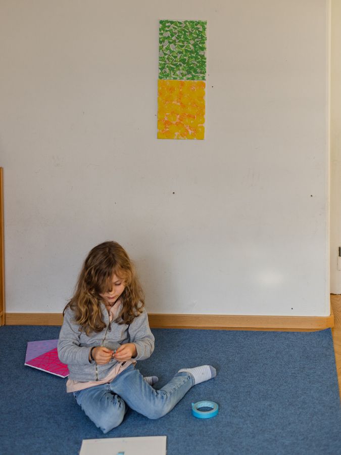 Mädchen sitzt vor einer Wand, auf der ein gelbes und ein grünes Blatt kleben
