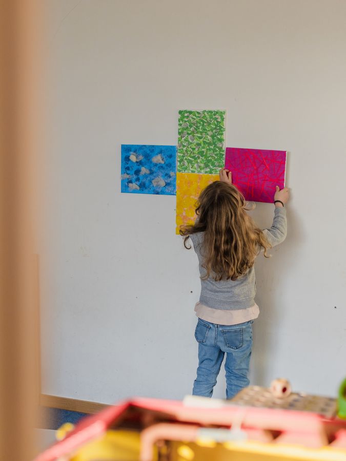 Ein Mädchen hängt ein Bild mit roter Farbe an eine Wand.