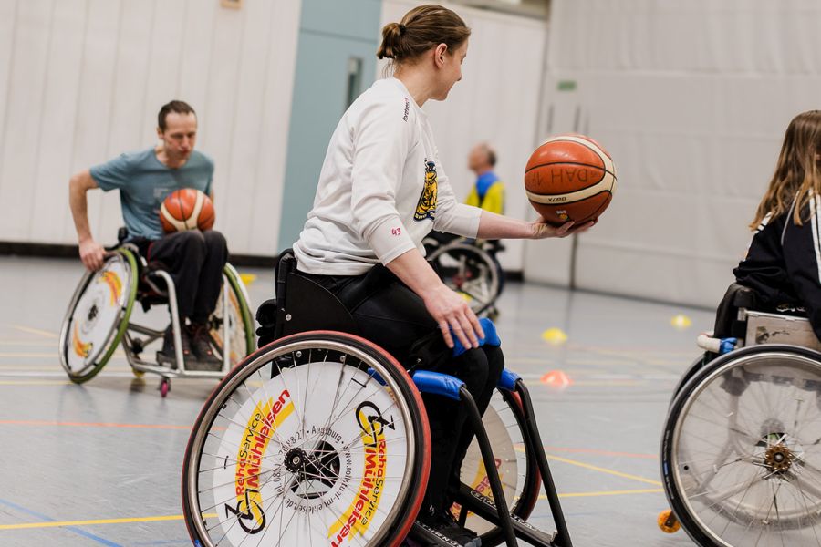 Junge Rollstuhlfahrerin hält den Basketball bei einem Spiel in einer Turnhalle