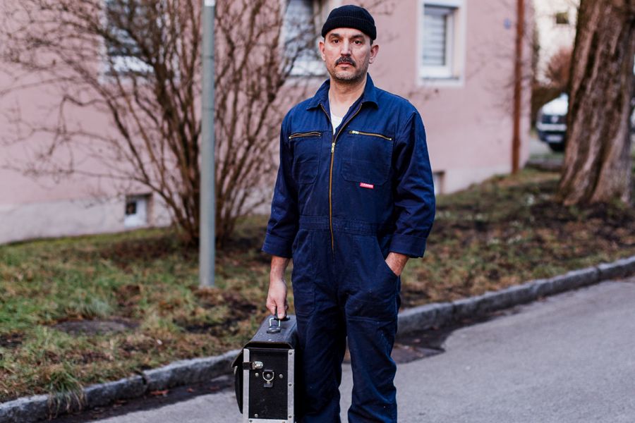 Ein Handwerker im Blaumann steht mit seiner Werkzeugtasche auf einem Gehweg