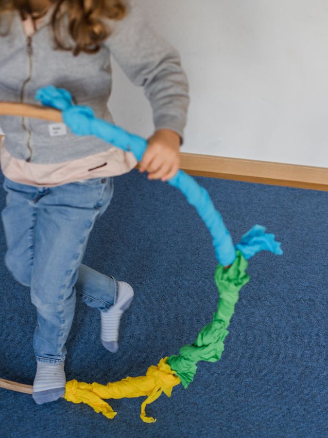 Mädchen spielt mit einem Reifen, der mit blauem Stoff umwickelt ist