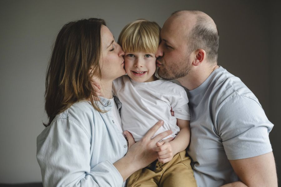 Mutter und Vater küssen ihren Sohn