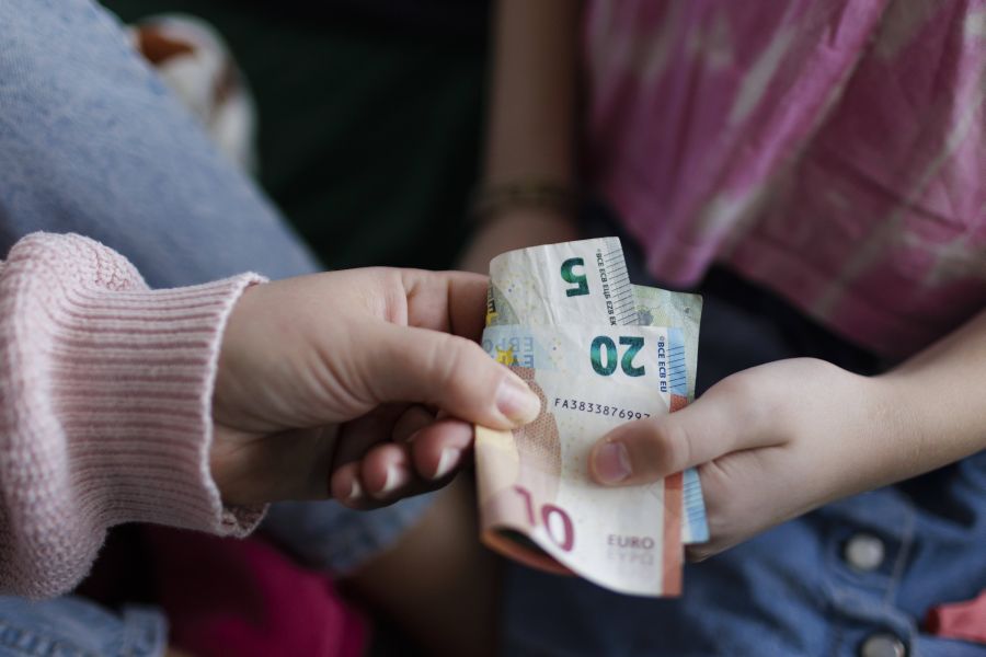 Eine Frauenhand gibt einer Kinderhand Geldscheine