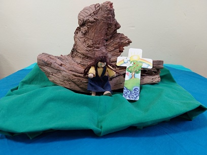Figur und buntes Kreuz vor einer Wurzel