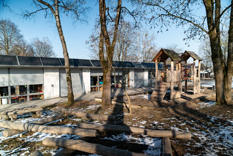 Gartenansicht der Kita St. Quirin mit Klettertürmen, Balanzier-Baumstämmen und Bäumen